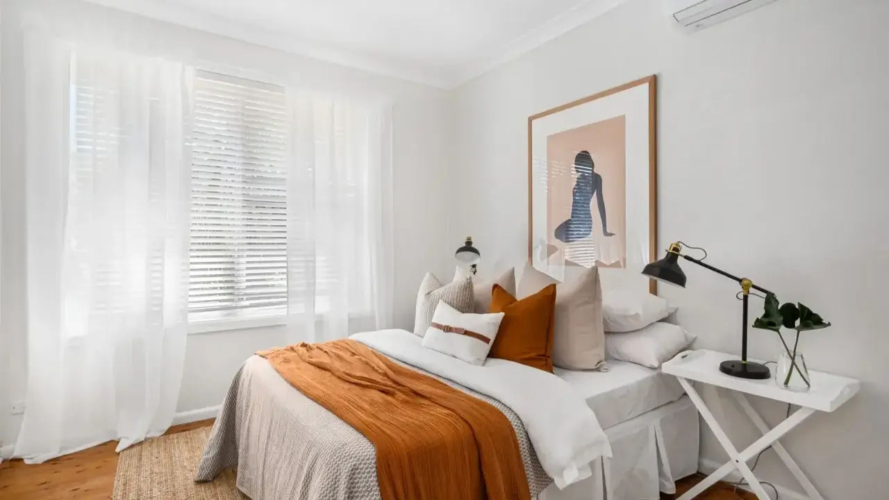 Une chambre confortable avec un lit douillet, des rideaux blancs et une unité de climatisation discrètement placée en hauteur, idéale pour savoir ou placer une clim dans une chambre.
