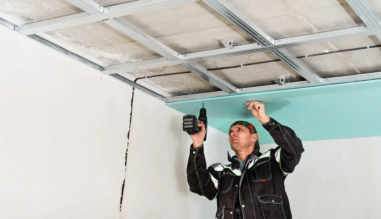 Un ouvrier installe des plaques de plâtre pour l'isolation du plafond de son garage.