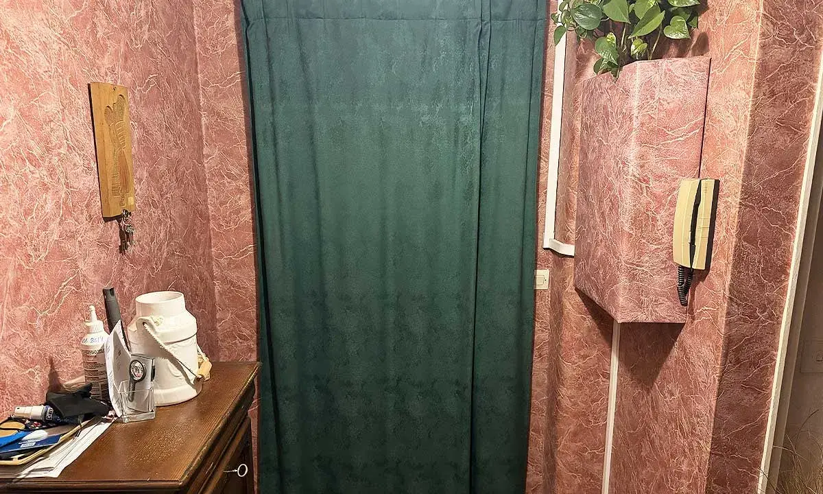 Rideau vert devant une porte, une idée pour comment isoler une porte. Meuble en bois, téléphone, plante verte.