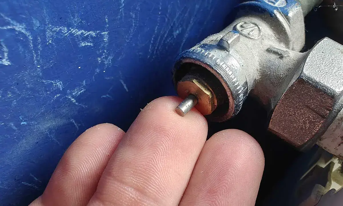 Main d'un doigt touchant la tige d'un robinet thermostatique bloqué chaud, avec une partie métallique visible.