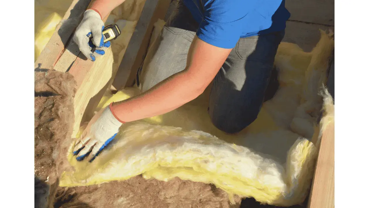 Pose d'isolant jaune entre les solives pour l'isolation plancher bas. Gants blancs et bleus, mètre en main.