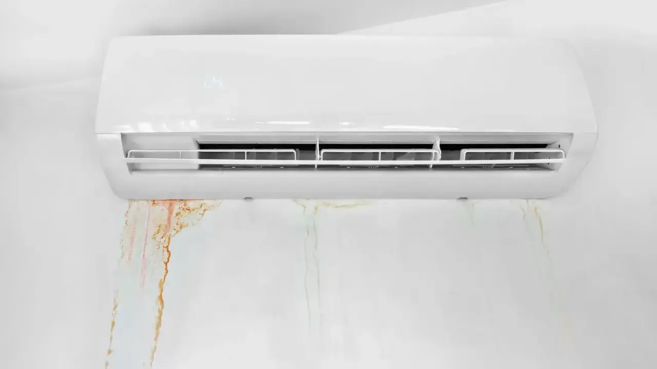 Clim qui coule : des traces d'eau rouille marquent le mur blanc sous un climatiseur.