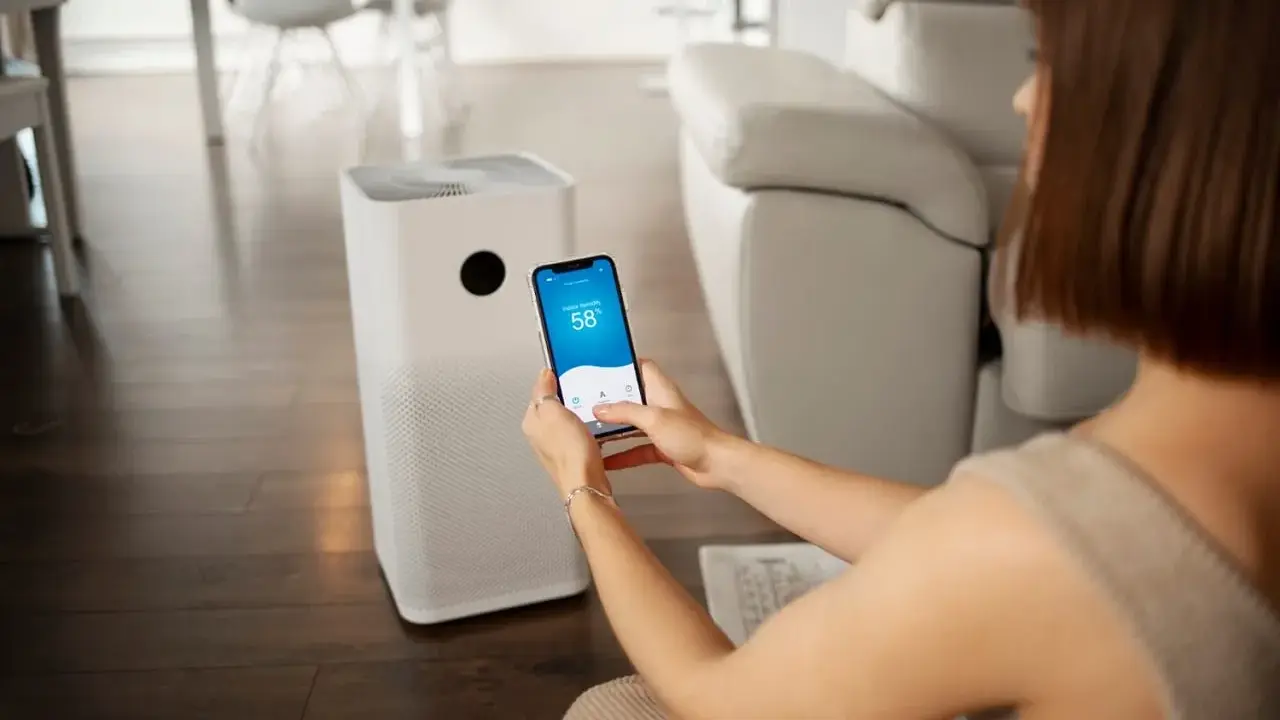 Une femme contrôle son climatiseur Proline via une application sur son smartphone, affichant 58% d'humidité intérieure.