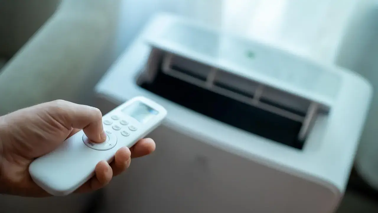 Main tenant utilise la télécommande pour régler son meilleur climatiseur mobile pas cher.