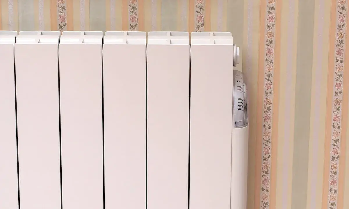 Un radiateur électrique à inertie blanc, avec son thermostat discret, se tient près d'un mur aux rayures pastel et fleuries.