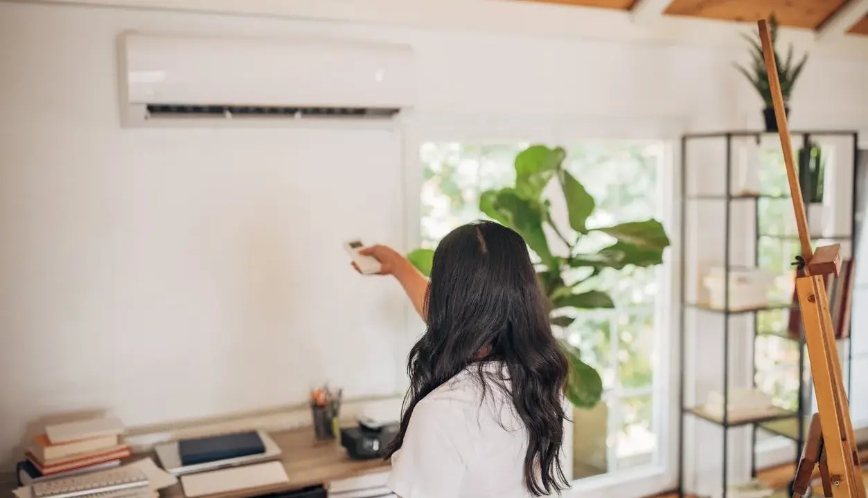 Une femme utilise une télécommande pour régler son climatiseur Mitsubishi Heavy Industries.