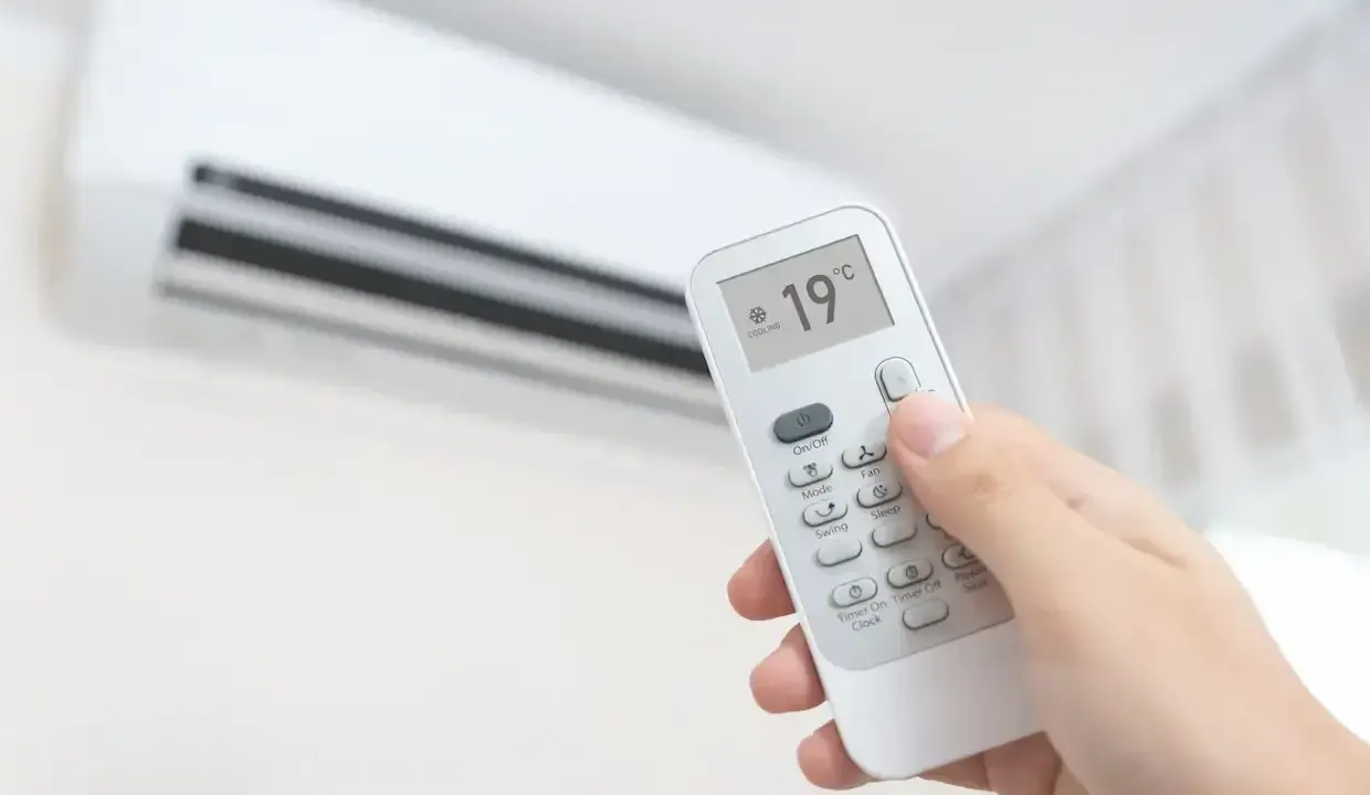 Main tenant ajuste la climatisation chaud à 19°C avec une télécommande.
