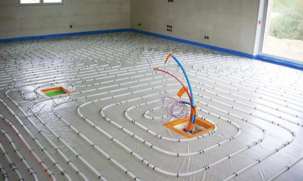 Installation de tubes pour un chauffage électrique au sol. Le sol est recouvert d'une bâche et les tubes blancs sont disposés en spirale.