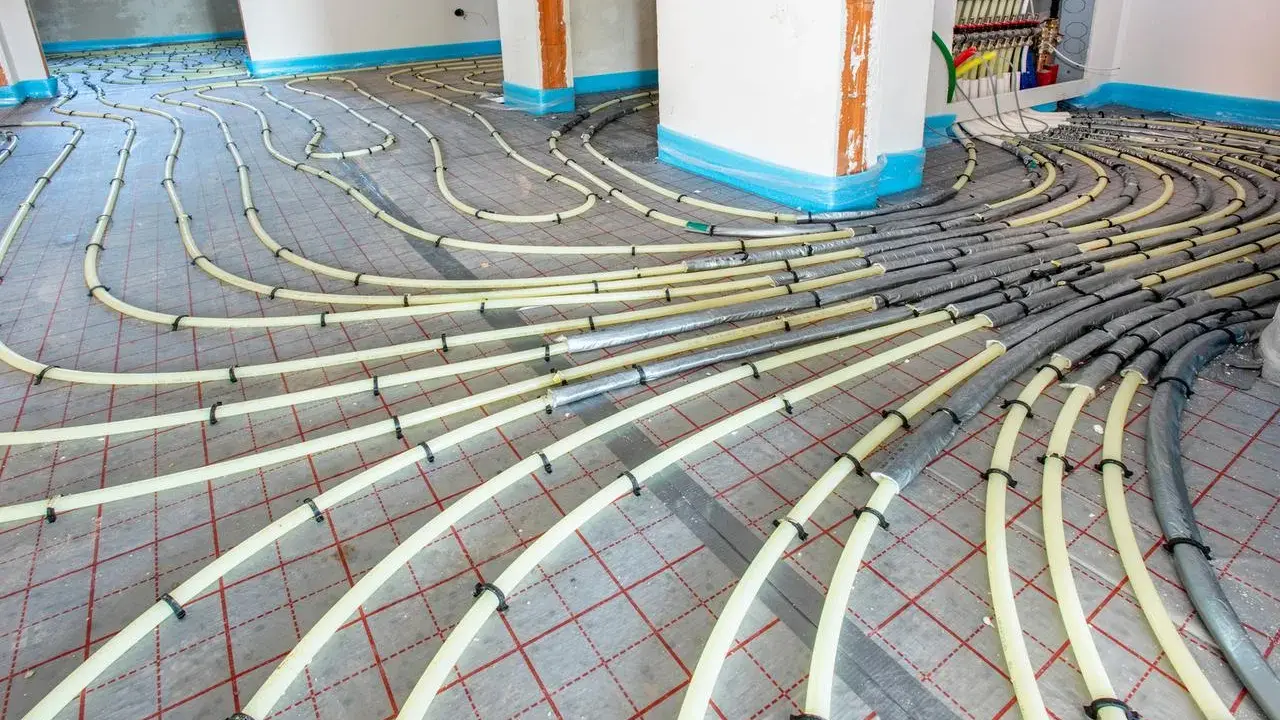 Installation de tubes pour un système de chauffage au sol. Les tuyaux jaunes sont fixés sur une grille rouge, prêts à être recouverts.