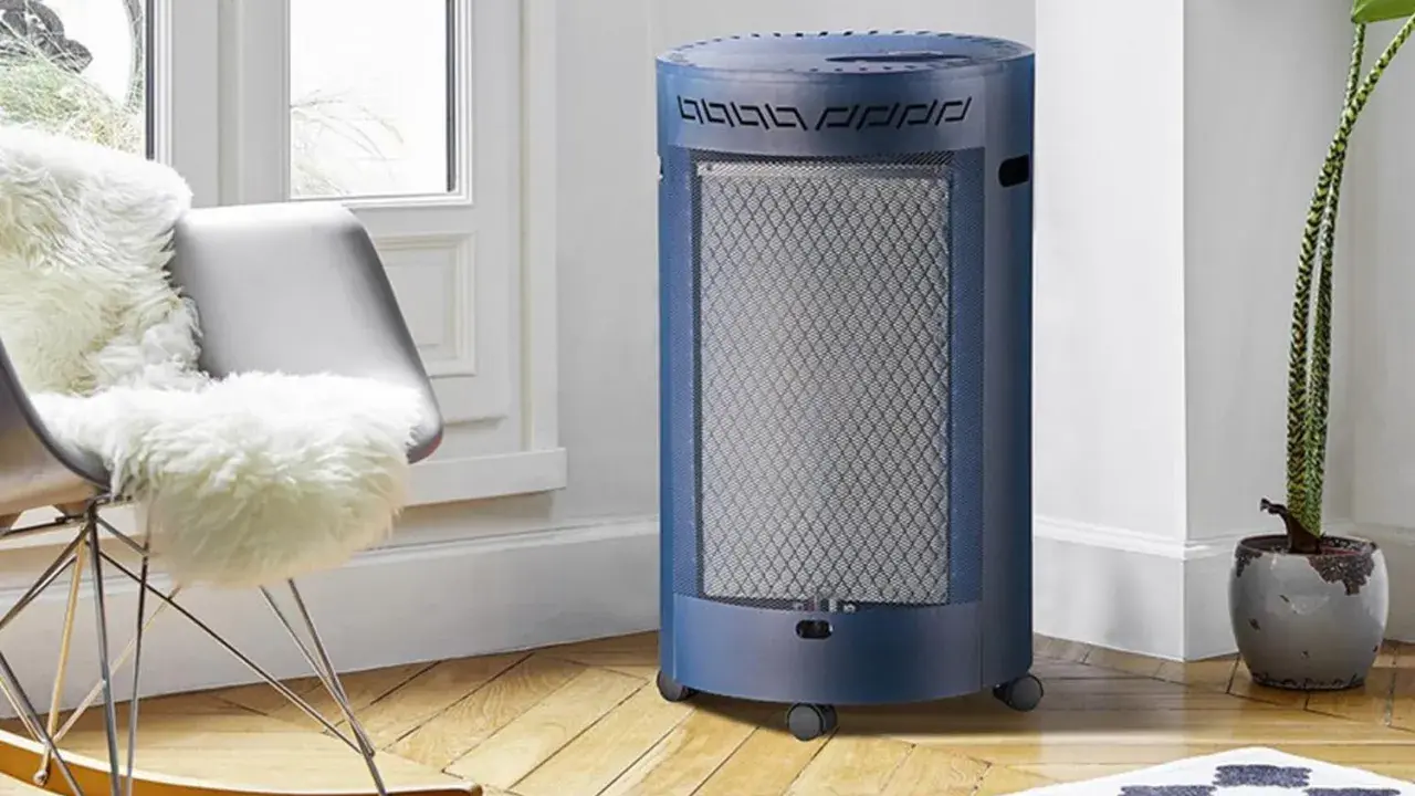 Un chauffage gaz infrarouge ou infrableu bleu, cylindrique et sur roulettes, diffuse sa chaleur dans un salon cosy, près d'un fauteuil confortable.