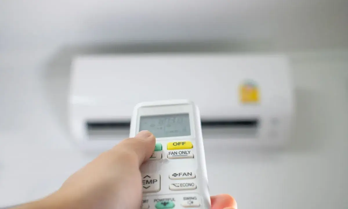 Main tenant utilise la télécommande pour régler la clim en été. La température est affichée sur l'écran.