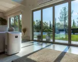 Climatiseur mobile 80m2 blanc, discret près d'un canapé, dans un salon lumineux avec vue sur jardin.