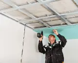 Un ouvrier installe des plaques de plâtre pour l'isolation du plafond de son garage.
