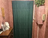 Rideau vert devant une porte, une idée pour comment isoler une porte. Meuble en bois, téléphone, plante verte.