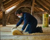 Un ouvrier installe de l'isolant dans des combles aménageables. Le prix au m2 de l'isolation des combles aménageables est un investissement pour le confort.