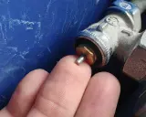 Main d'un doigt touchant la tige d'un robinet thermostatique bloqué chaud, avec une partie métallique visible.