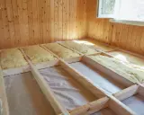 Travaux d'isolation plancher bois en cours. Laine de verre posée entre les solives en bois, prête pour la prochaine étape de construction.