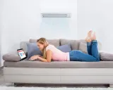 Une jeune femme détendue sur un canapé, profitant du confort d'un climatiseur triple split tout en faisant du shopping en ligne.