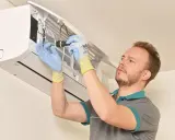 Technicien en gants bleus et jaunes effectuant la mise en service d'une clim split, outil à la main.