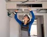 Installation d'un système de climatisation gainable plafond. Une ouvrière visse une plaque de plâtre.
