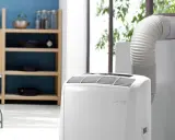 Climatiseur mobile blanc avec tuyau d'évacuation relié à une fenêtre.
