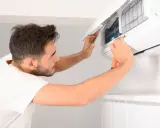Un homme nettoie une clim avec un tournevis. Il ouvre le capot pour accéder aux filtres.