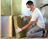 Un ouvrier installe un isolant minéral dans un mur. Pour une isolation par injection, le prix peut varier.
