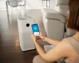 Une femme contrôle son climatiseur Proline via une application sur son smartphone, affichant 58% d'humidité intérieure.