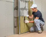 Un ouvrier installe un isolant minéral pour l'isolation mur intérieur. Le chantier progresse.