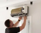 Un homme installe un climatiseur. Le tuyau d'évacuation de la clim qui chauffe est visible.
