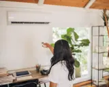 Une femme utilise une télécommande pour régler son climatiseur Mitsubishi Heavy Industries.