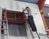 Un technicien sur une échelle nettoie un aérotherme de chauffage industriel.