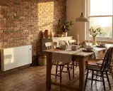 Chauffage moderne en pierre stéatite sur un mur de briques, réchauffant une salle à manger rustique avec une table en bois dressée.