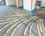 Installation de tubes pour un système de chauffage au sol. Les tuyaux jaunes sont fixés sur une grille rouge, prêts à être recouverts.