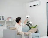 Un homme règle sa télécommande clim Toshiba en mode chauffage depuis son canapé.