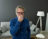 Homme d'âge mûr se pinçant le nez, visiblement incommodé par une mauvaise odeur de clim neuve dans son salon moderne.