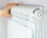 Main d'une personne ajustant un radiateur blanc, élément clé du système chauffage maison.
