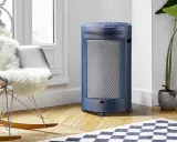 Un chauffage gaz infrarouge ou infrableu bleu, cylindrique et sur roulettes, diffuse sa chaleur dans un salon cosy, près d'un fauteuil confortable.