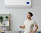 Un homme réfléchit à la question : faut-il laisser tourner une clim en permanence en mode chauffage ? Il tient une télécommande, regardant l'appareil mural.