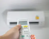 Main tenant utilise la télécommande pour régler la clim en été. La température est affichée sur l'écran.