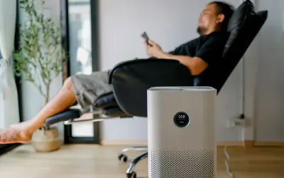 Un homme se repose dans un fauteuil, une plante verte à côté. Un purificateur d'air est au premier plan. Peut-on coucher une clim mobile ? Non, cet appareil est conçu pour rester debout.