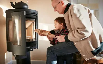 Un grand-père aide son petit-fils à charger du bois dans un poêle. Une alternative au chauffage au fioul, mais attention aux dangers du feu.