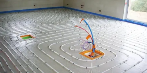 Installation de tubes pour un chauffage électrique au sol. Le sol est recouvert d'une bâche et les tubes blancs sont disposés en spirale.