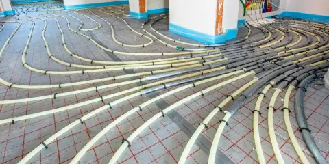Installation de tubes pour un système de chauffage au sol. Les tuyaux jaunes sont fixés sur une grille rouge, prêts à être recouverts.