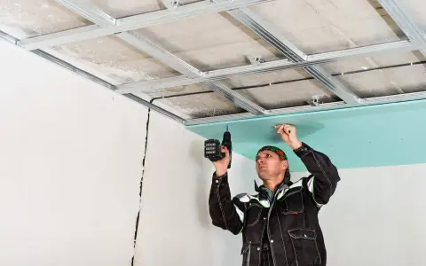 Un ouvrier installe des plaques de plâtre pour l'isolation du plafond de son garage.