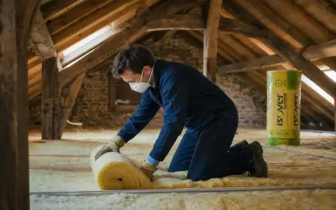 Un ouvrier installe de l'isolant dans des combles aménageables. Le prix au m2 de l'isolation des combles aménageables est un investissement pour le confort.
