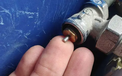 Main d'un doigt touchant la tige d'un robinet thermostatique bloqué chaud, avec une partie métallique visible.