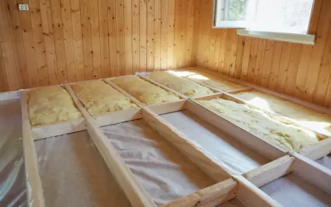 Travaux d'isolation plancher bois en cours. Laine de verre posée entre les solives en bois, prête pour la prochaine étape de construction.
