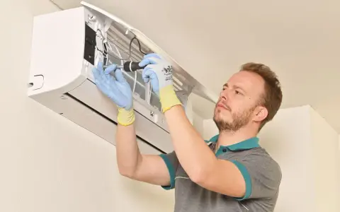 Technicien en gants bleus et jaunes effectuant la mise en service d'une clim split, outil à la main.