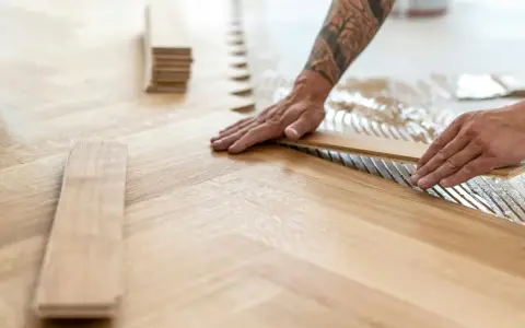 Pose de lames de parquet en bois, créant un motif en chevrons. L'isolation du sol est assurée par la colle appliquée.
